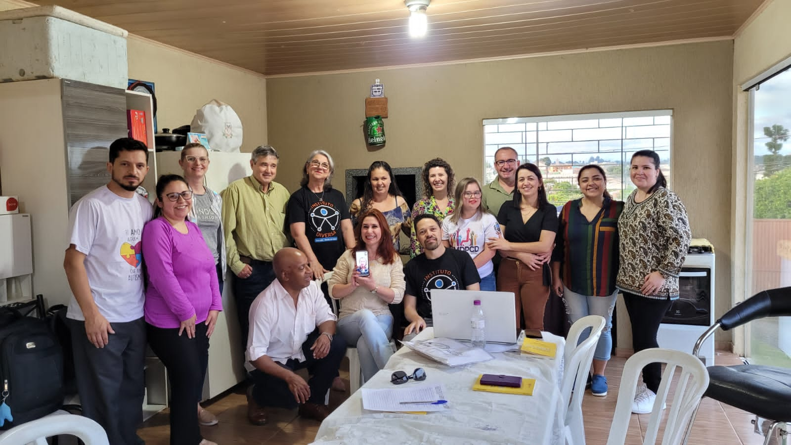 Descrição: Na foto consta várias pessoas em pé. A presidente Celia Carreira e o primeiro secretário Marcos Carreira estão sentados em duas cadeiras e o suplente do conselho fiscal Denival Luiz Oliveira está agachado. Todos estão em frente de uma churrasqueira.